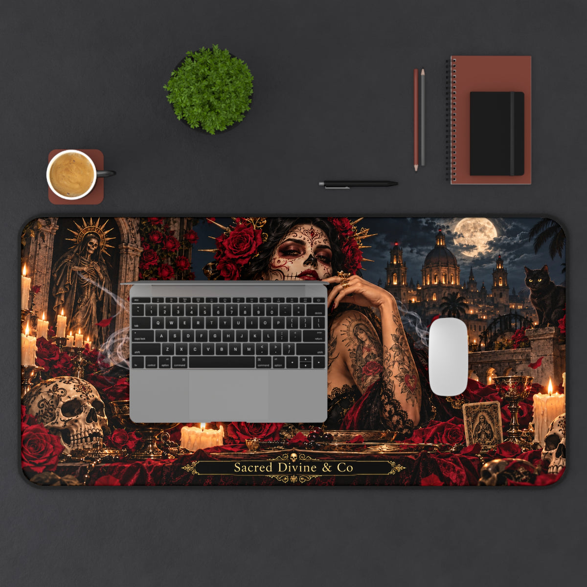 Gothic Day of the Dead desk mat showing sugar-skull woman with red roses against moonlit architecture, arranged horizontally on a desk beneath a laptop with a mouse, plant, cup, and notebook.