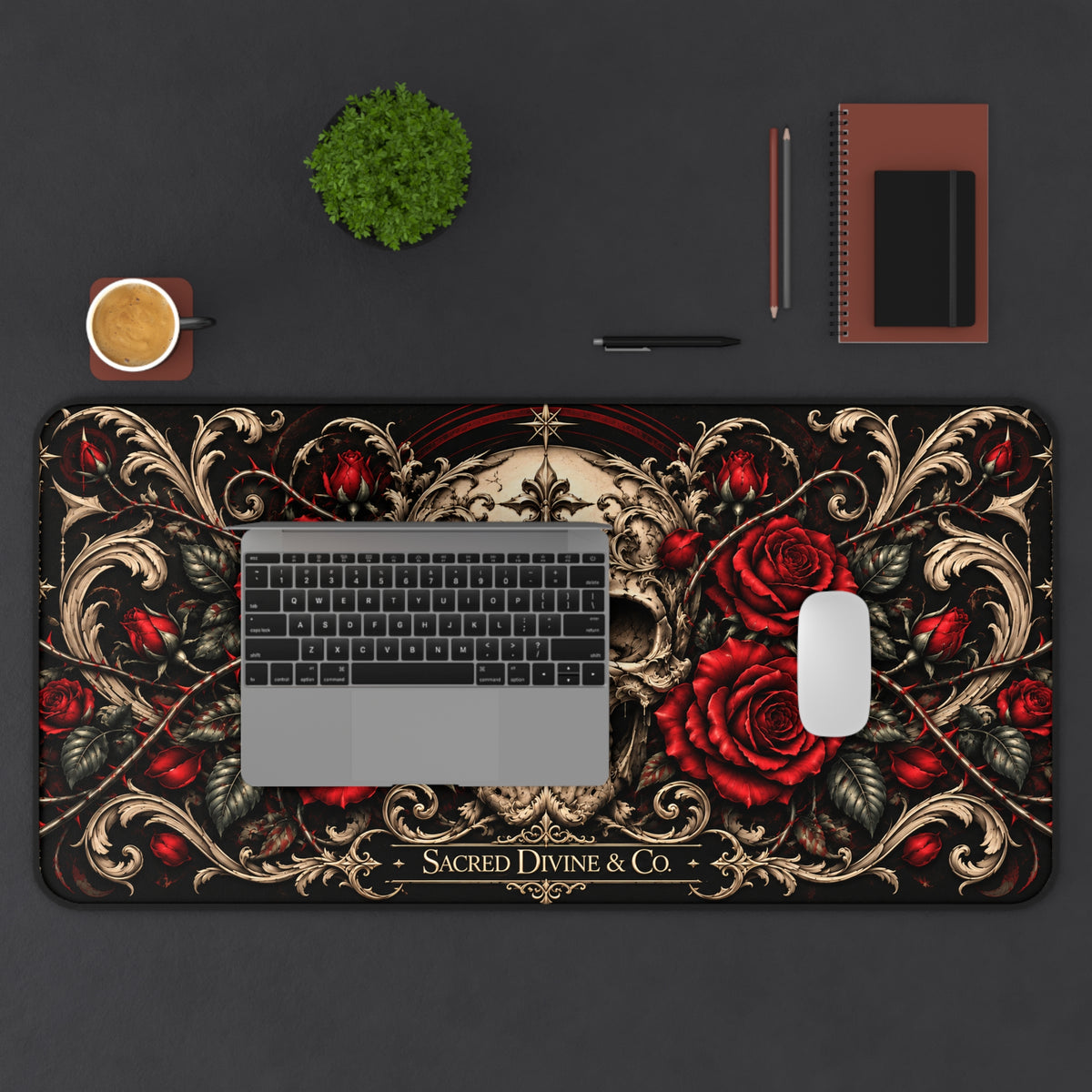 Gothic Skull and Red Roses desk mat showing centered skull framed by ornate cream scrollwork, arranged horizontally on a desk beneath a laptop with a mouse, plant, cup, and notebook.