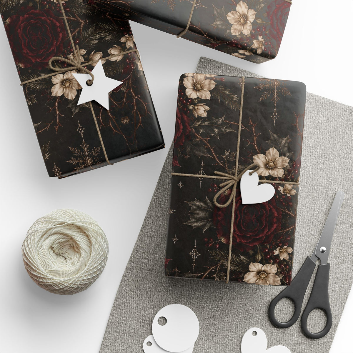 Several gifts wrapped in Dark Vintage Floral paper with twine and tags, arranged beside scissors and a ball of twine.